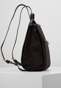 Czarny plecak wykonany z miękkiego zamszu i skóry, charakteryzujący się trójkątnym kształtem, dwiema regulowanymi ramiączkami oraz perłowymi akcentami na zamku.