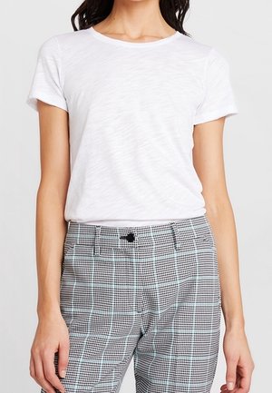 T-shirt blanc à manches courtes avec un col rond, texture lisse, associé à un pantalon taille haute à carreaux noir et blanc avec un détail de bouton noir.