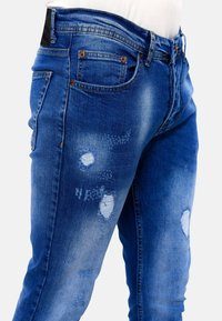 Blauwe denim jeans met een verstoord ontwerp; voorzien van scheuren en een lichte vervaging. Klassieke vijf-pocket stijl met contrasterende stiksels en een gladde textuur.