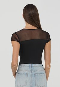 Body nero con maniche corte in rete trasparente, caratterizzato da una parte inferiore aderente e liscia e da uno schienale semplice, abbinato a pantaloni corti in denim chiaro.