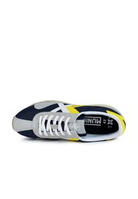 Zapatilla de color marino y gris con cordones blancos, que presenta acentos amarillos y grises, tejido texturizado y punta redondeada. Etiqueta de tamaño visible en el interior.