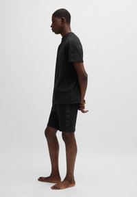 Musta lyhythihainen t-paita ja siihen sopivat shortsit, joissa on sileä rakenne sekä sävykkäät brändäys yksityiskohdat hihoissa ja shorttien sivuilla.