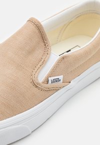 Bežne platnene cipelice u bež boji s bijelim gumiranim potplatom, s herringbone teksturom i malom Vans oznakom sa strane.