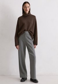 Brązowy, oversize'owy sweter z golfem, zestawiony z szarymi spodniami o szerokich nogawkach; gładka faktura i nowoczesna sylwetka z czarnymi botkami za kostkę.