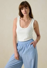 Witte tanktop met een ronde hals, gecombineerd met lichtblauwe, losvallende, gestructureerde broek met een elastische tailleband en zijzakken.