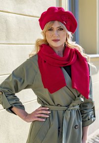 Red beret with floral detail and matching knit scarf, paired with a green trench coat featuring buttons and a tied belt.