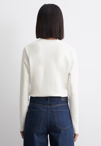 Hvid skjorte med lange ærmer lavet af blødt bomuldsstof, parret med mørkeblå højtaljede jeans, der har synlige baglommer og syninger.