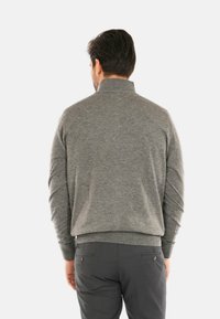 Maglione grigio con colletto alto, realizzato in un morbido tessuto a maglia. Caratterizzato da una vestibilità rilassata e polsini a coste, abbinato a pantaloni grigio scuro.