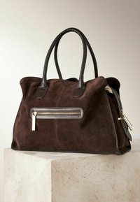 Bruine suede handtas met donkerleren accenten, twee handvaten en een voorzijde met ritsvak met gouden hardware. Geweven en ruime design.