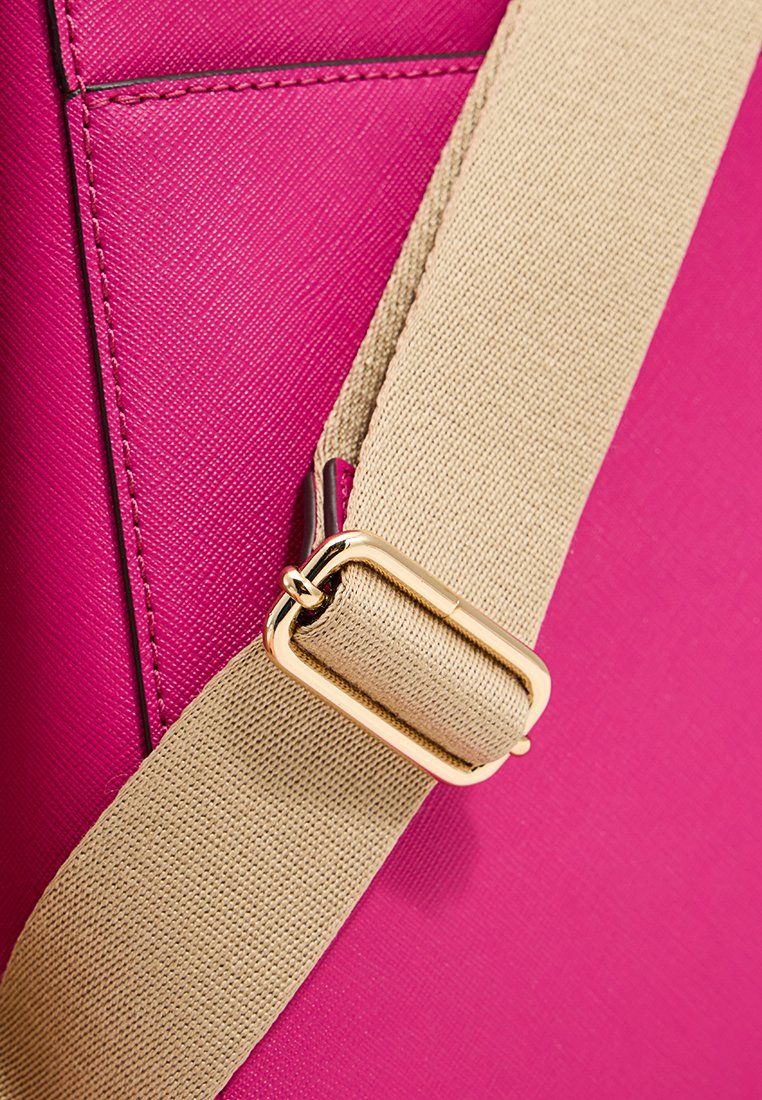 Fuchsia tas met een textuurafwerking, voorzien van een tan schouderband met een gouden metalen gespsluiting en stikseldetails aan de buitenzijde.
