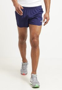 Námořnické sportovní šortky s elastickým pasem, vyrobené z lehkého materiálu, v kombinaci se šedými běžeckými botami s zelenými a růžovými akcenty.