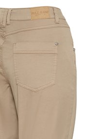 Beigenväriset Pulz-farkut, joissa on sileä pinta, yksi takatasku, logopatchi vyötäröllä ja vähäiset ompelut.