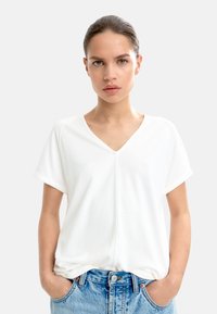 Hvid kortærmet V-hals t-shirt, lavet af glat stof, med en subtil søm ned langs midten. Kombineret med lyseblå jeans.