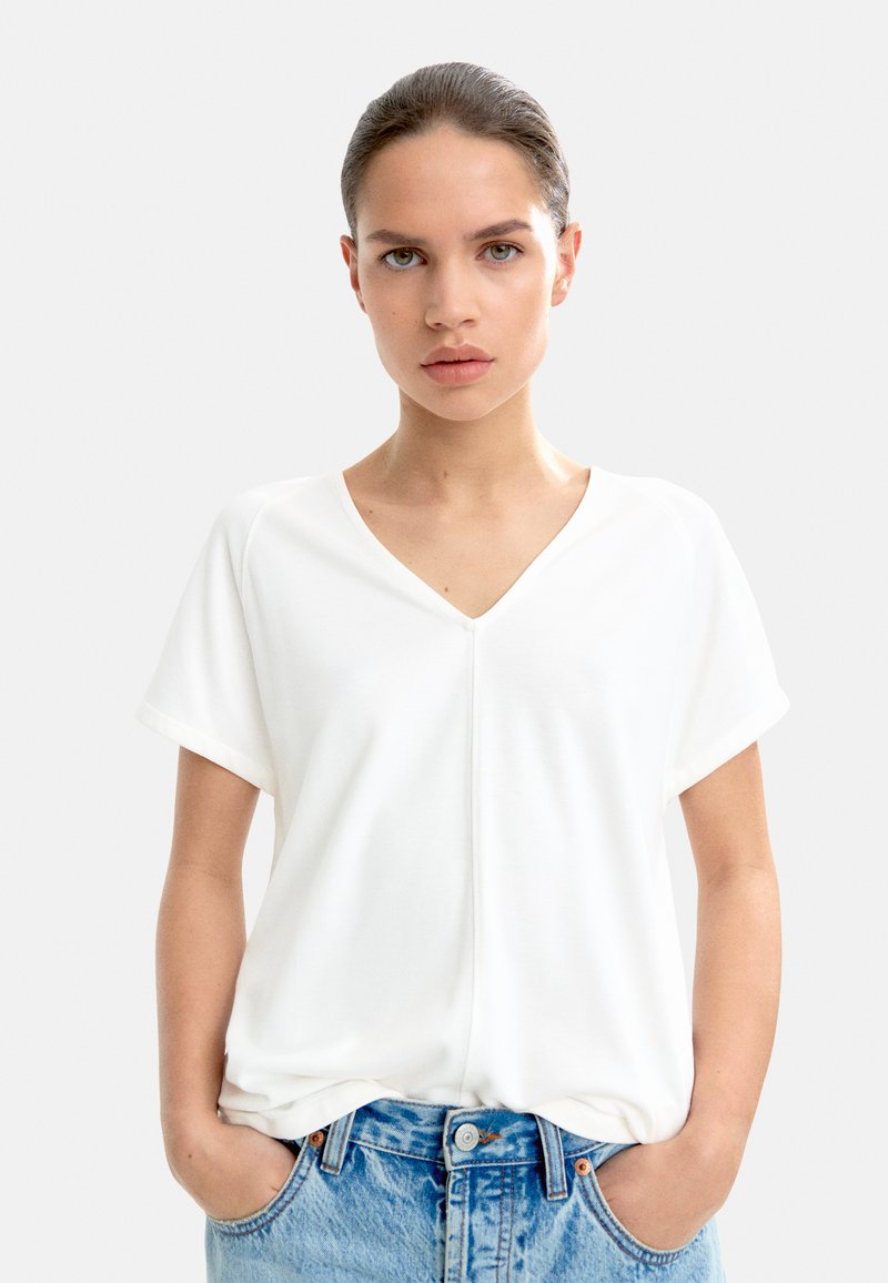 Hvid kortærmet V-hals t-shirt, lavet af glat stof, med en subtil søm ned langs midten. Kombineret med lyseblå jeans.
