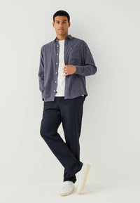 Blåternet skjorte med hvide knapper, båret over en hvid t-shirt. Sammen med marineblå bukser og hvide sneakers på en neutral baggrund.