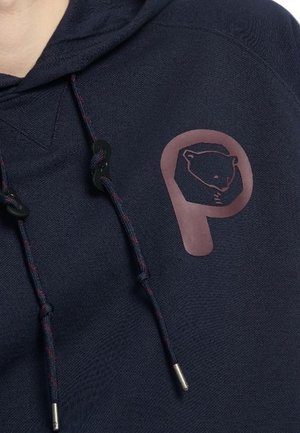 Donkerblauwe hoodie met zwarte en rode trekkoorden, met een grote roze "P"-logo met een dierengezicht erin op de borst.