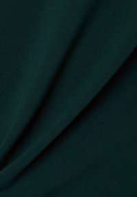 Teksturalna, ciemnozielona tkanina, prezentująca gęsty wzór splotu. Powierzchnia wydaje się miękka z subtelnymi fałdami, które nierównomiernie odbijają światło.