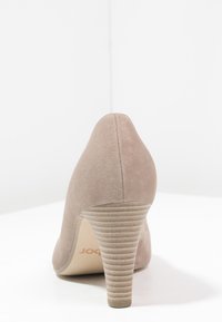 Beige ruskind højhælet sko med en fremadskridende design, struktureret hæl og glat overflade. Har en rund tå og subtile syninger.