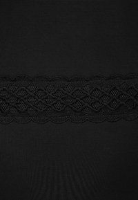 Czarna tkanina z teksturową koronkową lamówką o falbaniastym brzegu, tworzącą kontrast w wzorze i designie. Gładki ogólny wygląd.