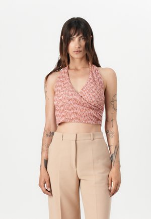 Top halter tricotat într-un model texturat de corali, cu lungime scurtă, asociat cu pantaloni bej cu talie înaltă. Tatuaje vizibile pe brațe.