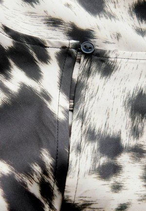 Must-valge mustriga kangas, millel on sile tekstuur, sisaldab nupudetaili tasku lähedal, esitledes kaasaegset disaini ja kohandatud viimistlust.