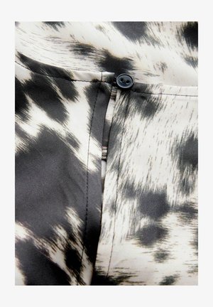 Un tissu à motif noir et blanc avec une texture douce présente un détail de bouton près d'une poche, mettant en avant un design moderne et une finition soignée.