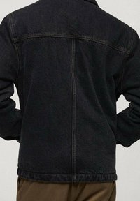 Chaqueta de mezclilla negra con corte recto, costuras visibles y cuello. Cuenta con mangas largas y un dobladillo que llega a la cintura.