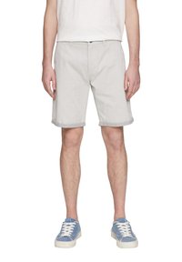 Lichtgrijze katoenen shorts met een opgerolde zoom, voorzien van broekzakken aan de voorkant en een tailleband met knoopsluiting, gecombineerd met blauwe sneakers.