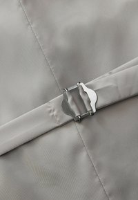 Tessuto grigio con una superficie liscia, dettagli in fibbia metallica, cuciture a vista e una forma piatta e rettangolare.