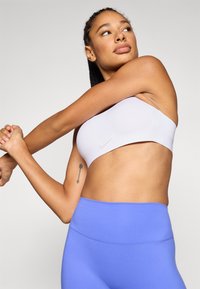 Witte sportbeha met een minimalistisch design en subtiel Nike-logo, gecombineerd met lichtblauwe leggings met hoge taille, beide gemaakt van glad materiaal.