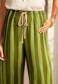 Groene gestreepte broek van een gestructureerde stof, met een lichtroze trekkoord in de taille en een wijde pasvorm. Accenten van lichte strepen.