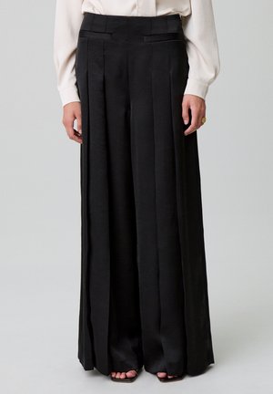 Pantalons larges noirs en tissu lisse et léger. Comprennent des poches latérales et des plis marqués, avec une taille ajustée.