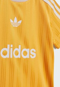Maglia sportiva gialla realizzata in tessuto strutturato, con righe verticali e logo 'adidas' bianco con tre strisce sulle spalle.