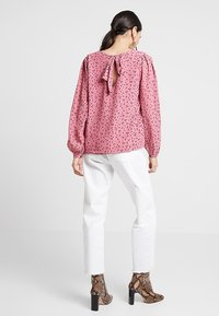 Roze blouse met lange mouwen, bloemenprint, strikdetail op de rug, ronde hals, ballonmouwen, gecombineerd met witte broek en slangenprint hakken.