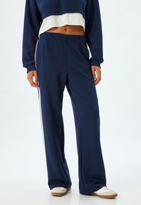 Marineblaue Jogginghose mit lockerem Schnitt, die einen weißen Streifen an der Seite, einen elastischen Bund und eine weiche Stoffstruktur aufweist.