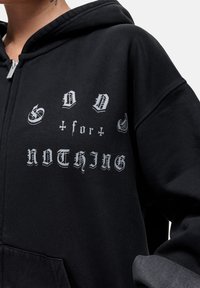 Felpa nera con cappuccio, caratterizzata da un grande testo argento in stile gotico che recita "GOD for NOTHING". Il materiale sembra morbido; design con cappuccio e tasca frontale.