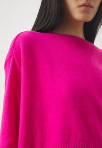 Helles pinkes Sweatshirt mit glatter Textur, weitem Ausschnitt und geripptem Saum. Aus Strickstoff mit lockerer Passform, die die lebendige Farbetonung zur Geltung bringt.