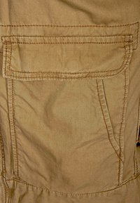 Khakifärgad tyg med en strukturerad yta och synliga stygn. Har en enda klaffficka framtill, vilket betonar praktisk användning och hållbarhet.