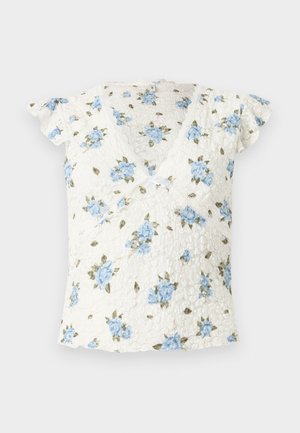 Haut court en dentelle blanche avec imprimé floral bleu, décolleté en V style cache-cœur et petit nœud au centre devant.