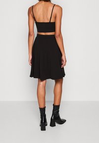 Černý zkrácený top bez rukávů v kombinaci s černou rozšířenou sukní, nošený s černými vysokými kozačkami na podpatku. Hladký materiál a dobře padnoucí střih.