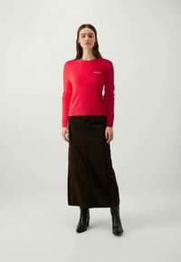 Red knitted sweater with a round neck, paired with a long, dark brown denim skirt. Black ankle boots complete the outfit.