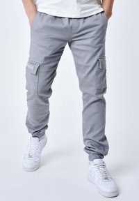 Pantalones cargo grises con puños elásticos, que cuentan con bolsillos laterales y un tejido suave y duradero. Combinados con zapatillas blancas para contrastar.