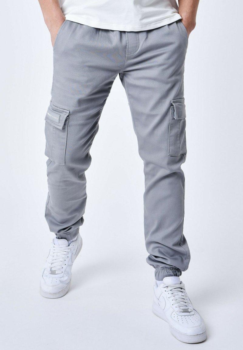 Pantalones cargo grises con puños elásticos, que cuentan con bolsillos laterales y un tejido suave y duradero. Combinados con zapatillas blancas para contrastar.