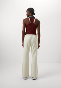 Top sin mangas color burdeos con tirantes en contraste y pantalones de pierna ancha color crema que cuentan con una cinturilla elástica, textura suave y un corte relajado.
