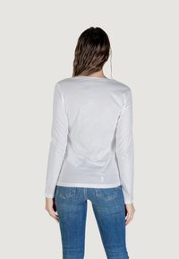 Maglietta a maniche lunghe bianca in cotone morbido, con colletto rotondo e vestibilità aderente, abbinata a jeans in denim blu.