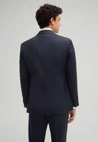 Giacca da abito blu navy con vestibilità su misura. Presenta uno spacco singolo, revers a motivo a U e bottoni neri sui polsini. Tessuto dalla finitura liscia.