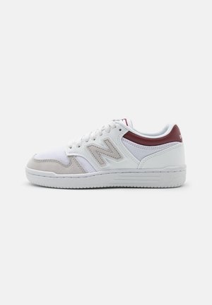 Baskets New Balance blanches et grises avec un accent bordeaux au talon, détails en mesh et en suède, et fermeture à lacets sur un fond uni.