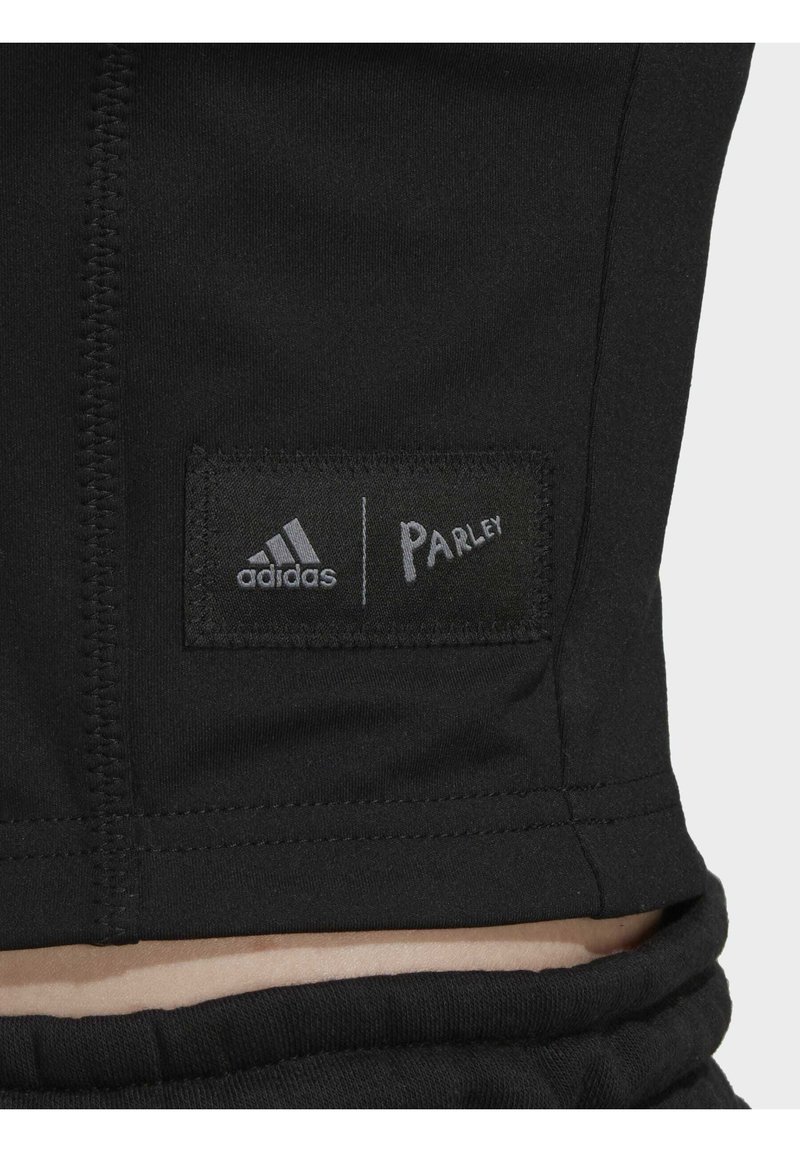 Schwarzer Stoff mit einem gestickten rechteckigen Aufnäher, der die Logos von adidas und Parley zeigt, auf dem unteren Rücken nahe der Taille.