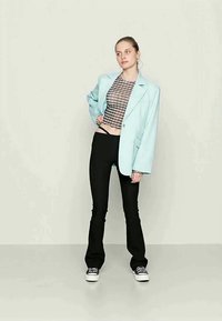 Blazer oversize azul claro sobre um top xadrez curto, combinado com calças pretas largas e ténis pretos. Textura suave e corte ajustado.