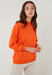 Orange sweatshirt with a high neckline, long sleeves, and ribbed hem. Smooth fabric with a relaxed fit and dropped shoulders.